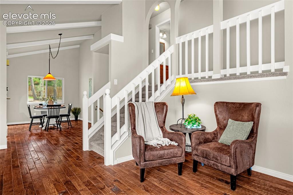 Image 7 of 40: Vaulted ceiling room with hardwood flooring, two large windows, light gray 