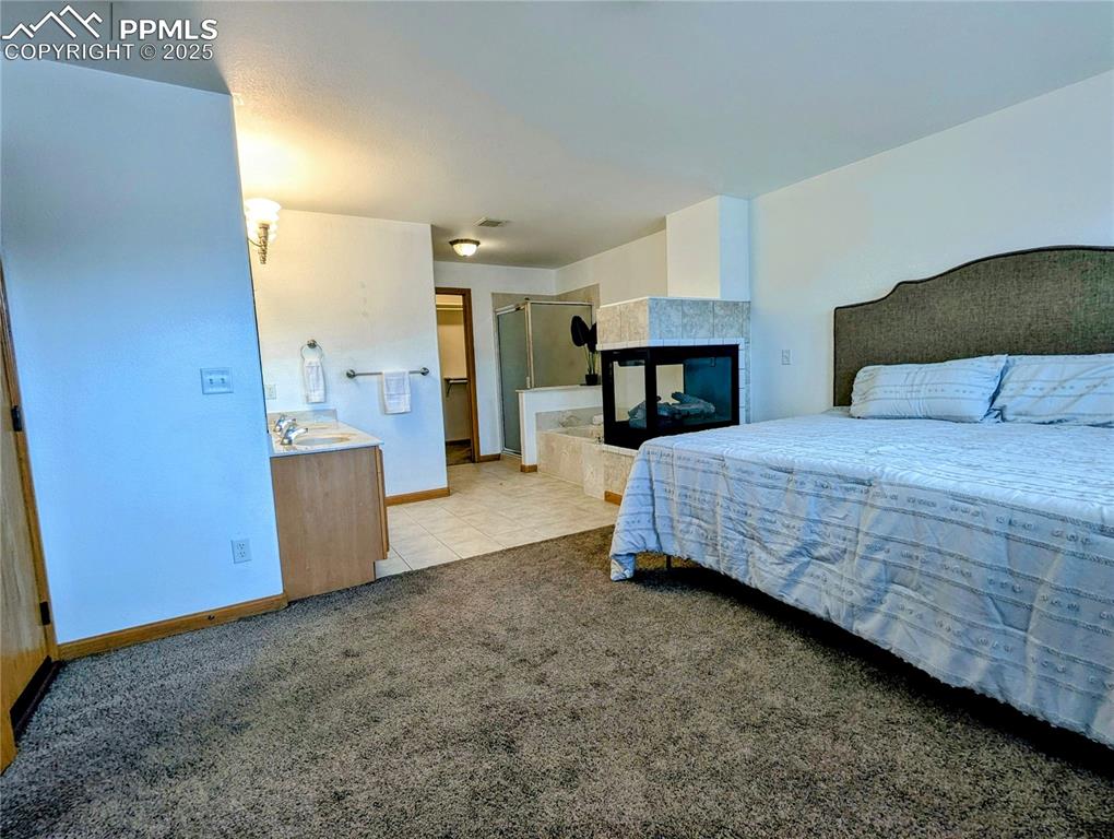 Image 14 of 19: Carpeted bedroom with a tile fireplace and tile patterned floors