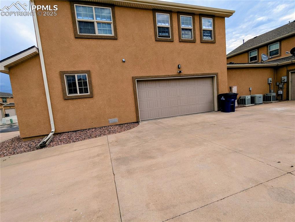 Image 18 of 19: Rear view of property featuring an attached garage, driveway, and stucco si
