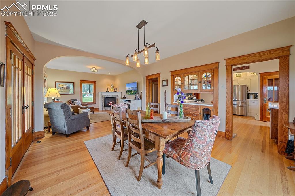 Image 11 of 44: Dining space with arched walkways, light wood-style flooring, and a lit fir