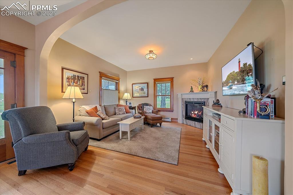 Image 13 of 44: Living room with a tiled fireplace, light wood finished floors, arched walk
