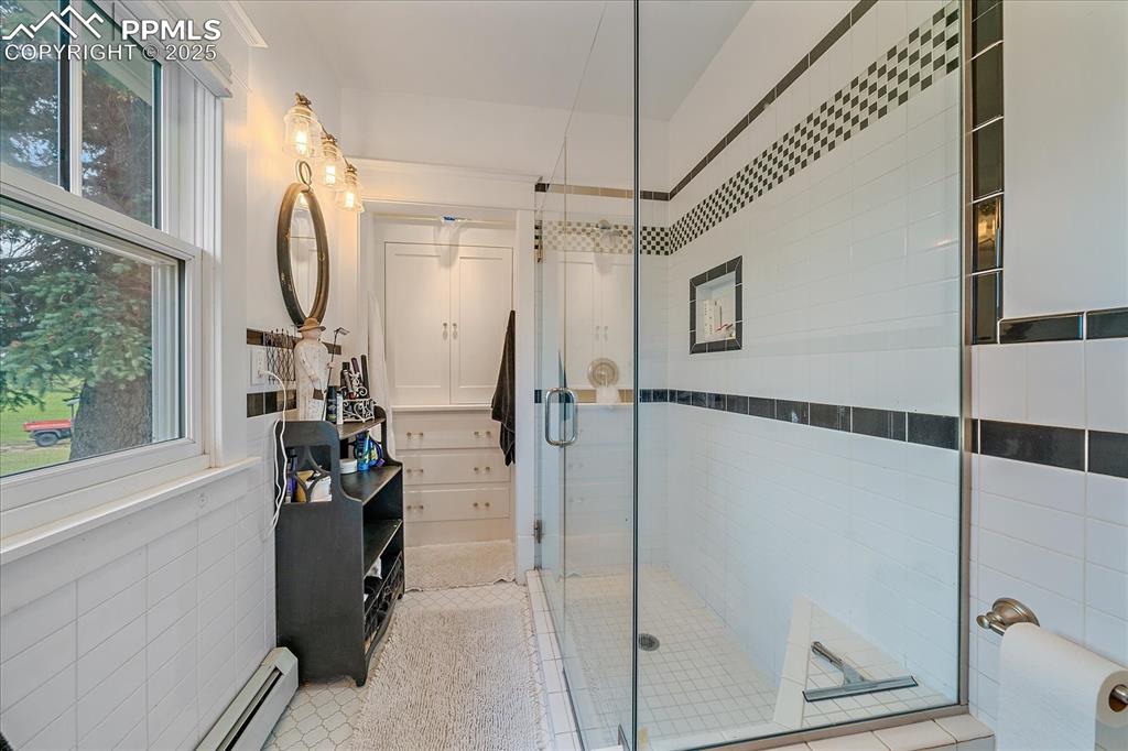 Image 18 of 44: Bathroom with a stall shower, a baseboard heating unit, tile walls, and til