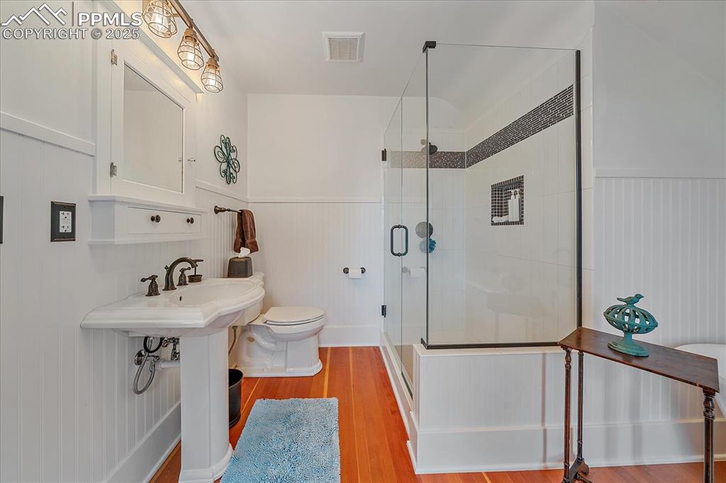 Image 24 of 44: Full bathroom with a stall shower, wainscoting, wood finished floors, and a