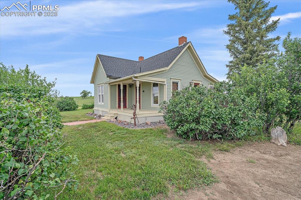 Image 26 of 44: View of side of property with a porch, a yard, a shingled roof, and a chimn