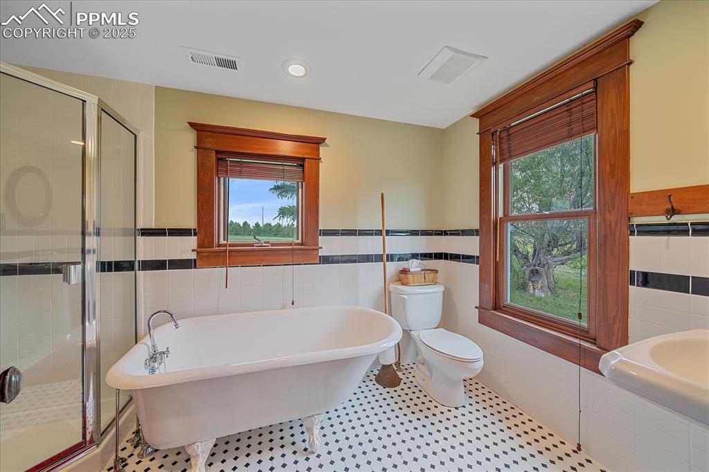 Image 31 of 44: Bathroom featuring tile walls, a freestanding bath, healthy amount of natur