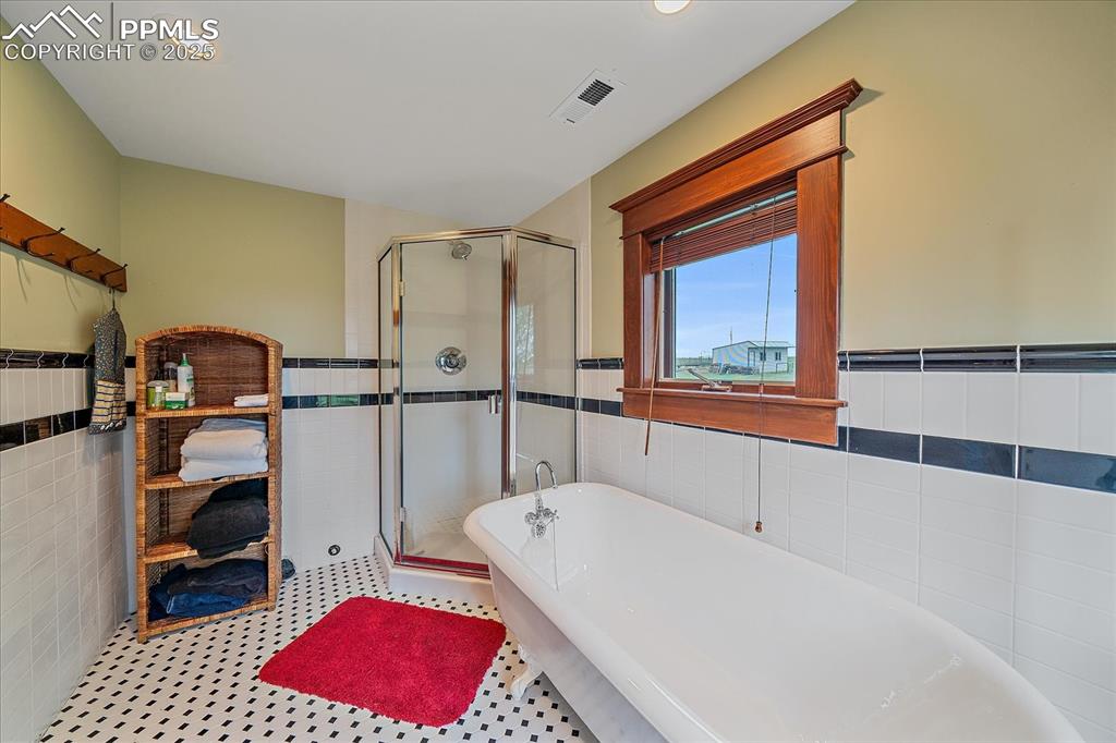 Image 32 of 44: Full bathroom with tile walls, a freestanding bath, a stall shower, a wains