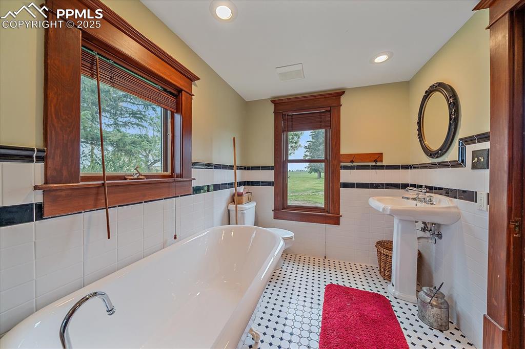 Image 33 of 44: Full bath with tile walls, a freestanding tub, a wainscoted wall, and reces