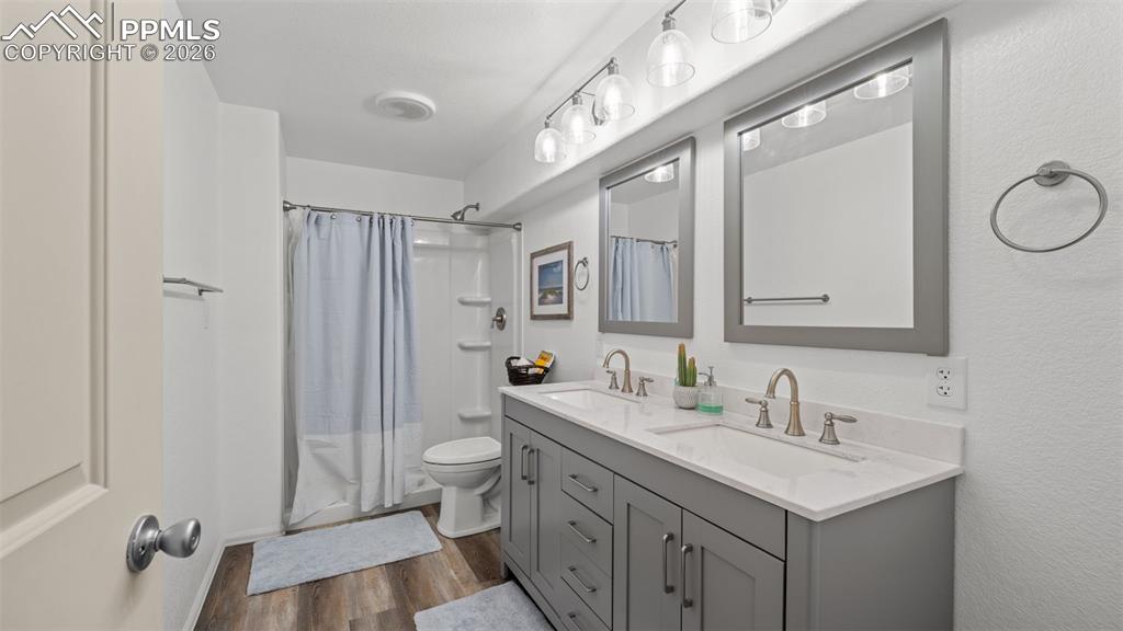 Image 16 of 28: Bathroom with double vanity, dark wood-style flooring, and shower / bath co
