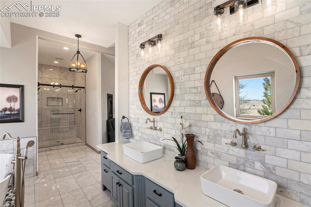 Image 16 of 47: Bathroom featuring a stall shower, double vanity, a chandelier, light marbl