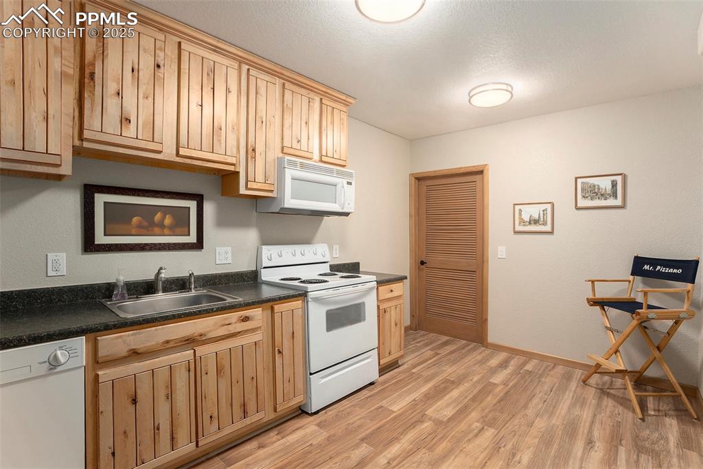 Image 30 of 47: Kitchen featuring white appliances, dark countertops, light wood-style floo