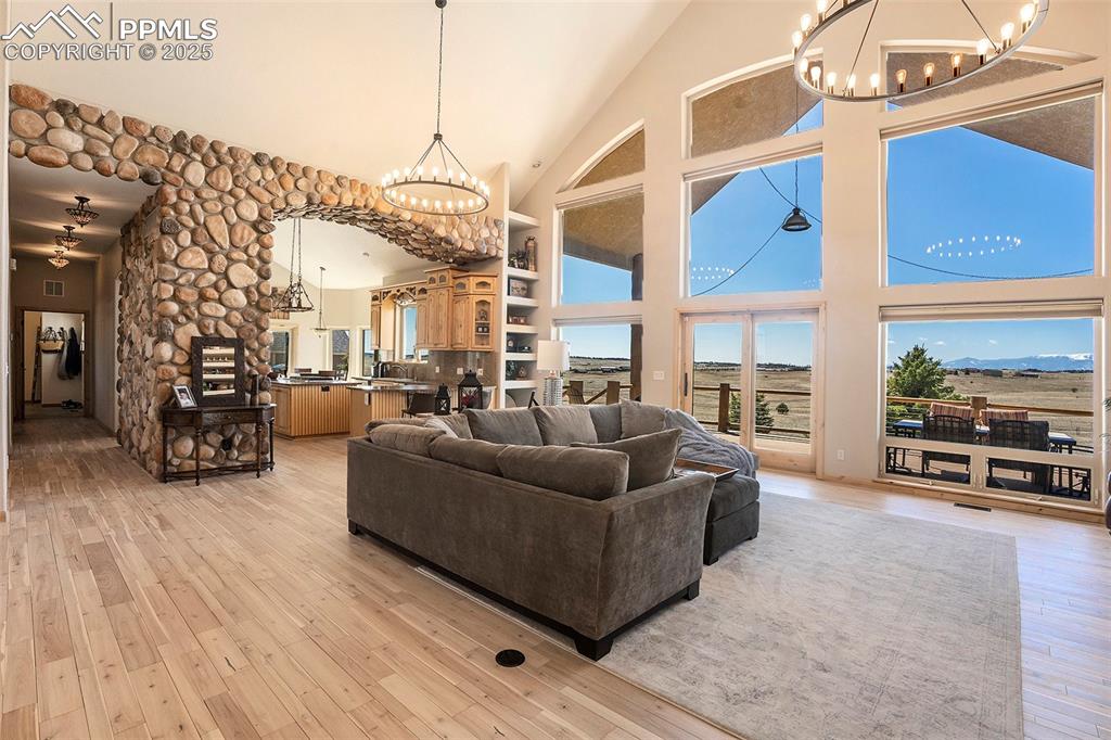 Image 7 of 47: Living area with a chandelier, high vaulted ceiling, and light wood-style f