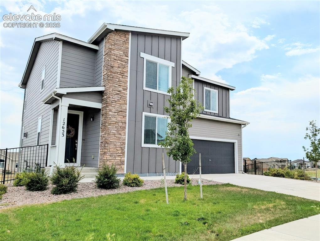 Caption: Stone accent pillar, vertical siding, two-car garage, concrete driveway, and front landscaping