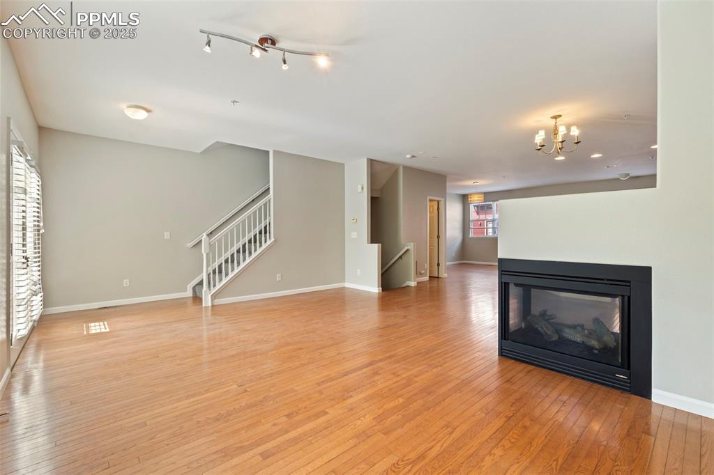Image 10 of 48: Unfurnished living room with stairs, light wood finished floors, a chandeli