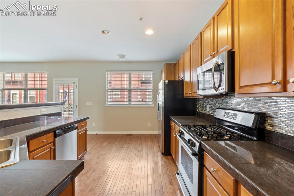 Image 12 of 48: Kitchen with stainless steel appliances, backsplash, light wood-style floor
