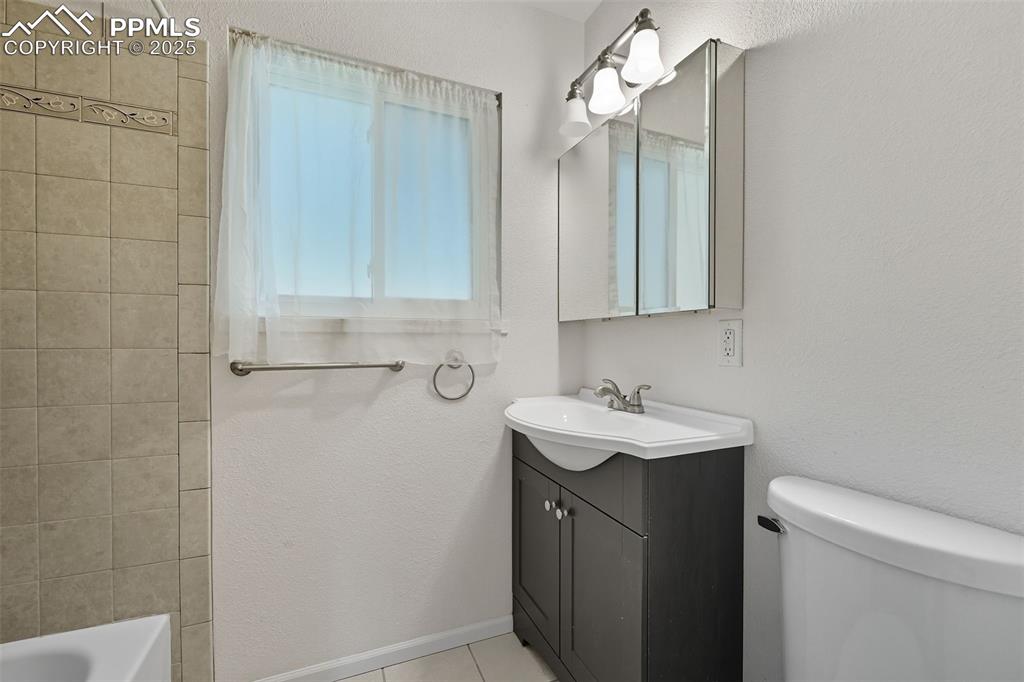 Image 11 of 29: Upper bathroom with a textured wall, vanity, and light tile patterned floor
