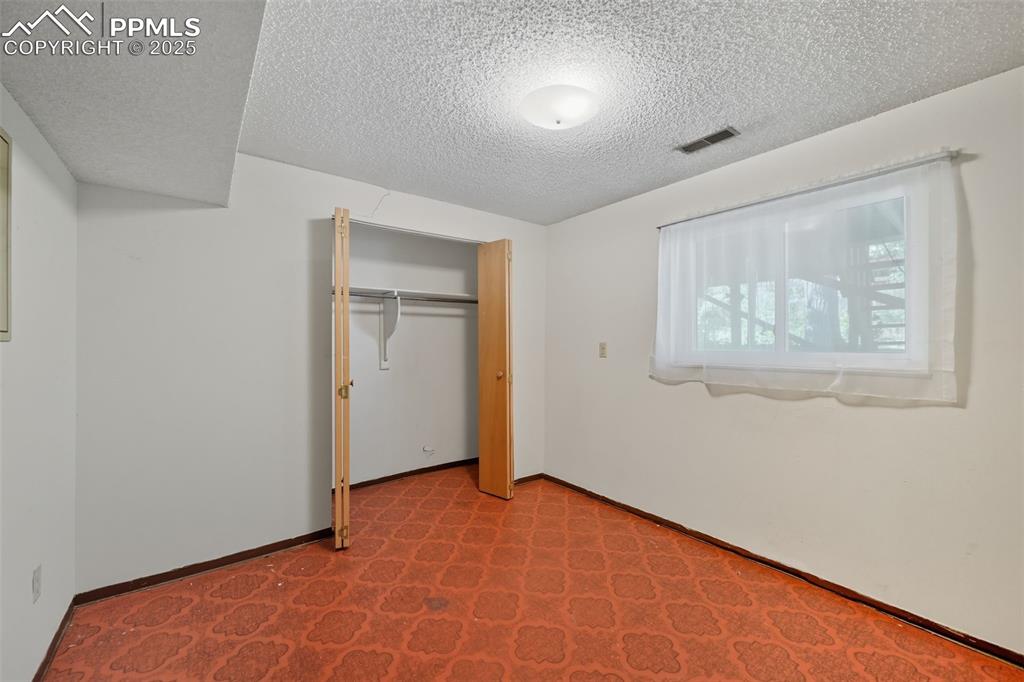Image 14 of 29: Lower bedroom 1 featuring a textured ceiling, a closet, and carpet floors
