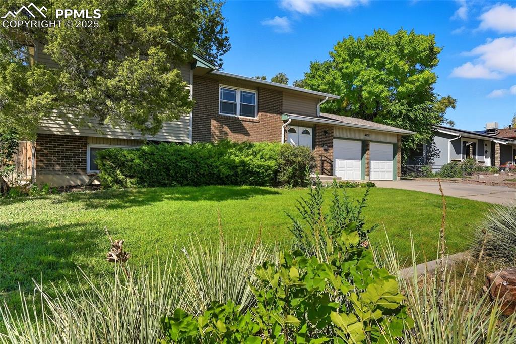 Image 29 of 29: Tri-level home with brick siding, a front lawn, driveway, and an attached g