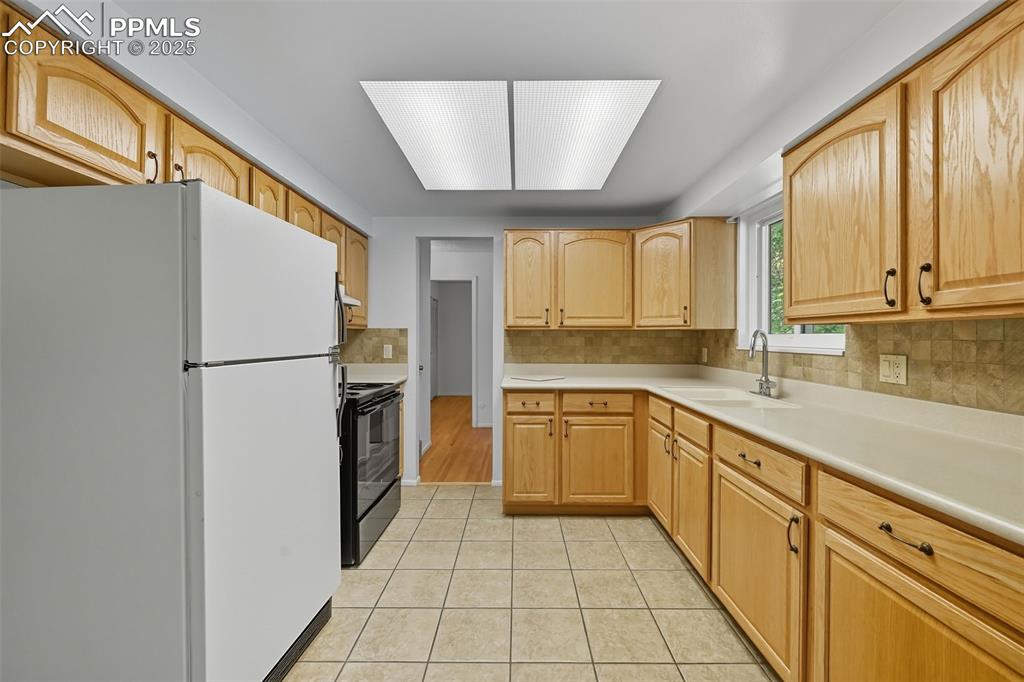 Image 5 of 29: Kitchen featuring freestanding refrigerator, light countertops, black range