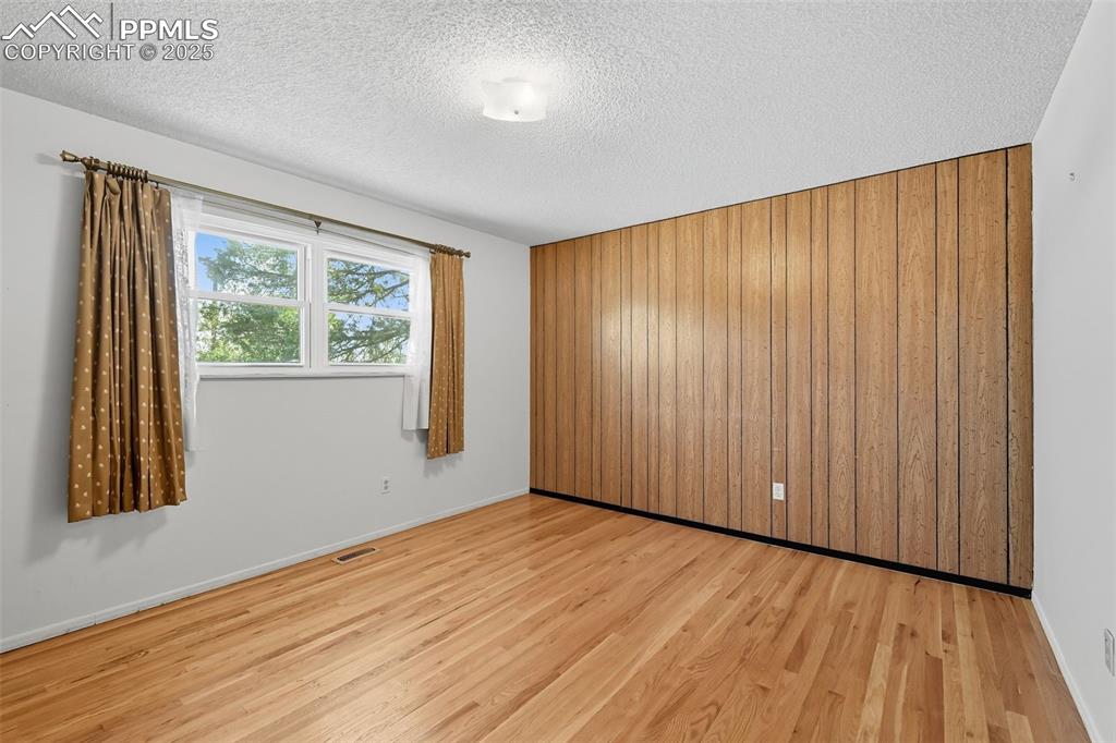 Image 9 of 29: Primary upper bedroom featuring wood walls, light wood floors, and a textur