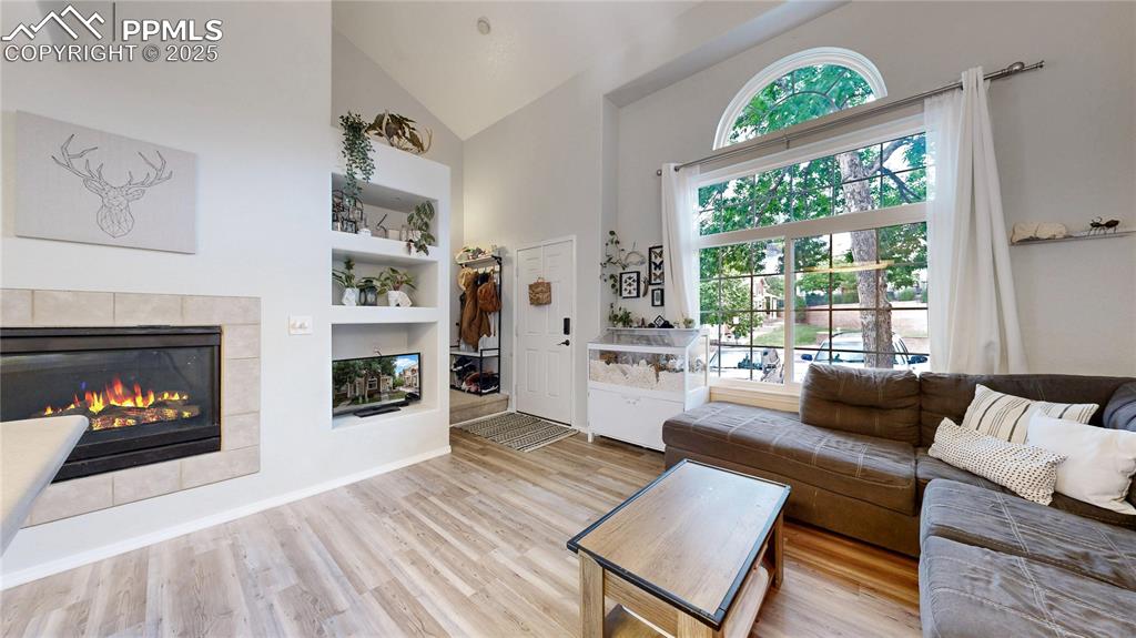 Image 6 of 37: Living room featuring high vaulted ceiling, wood finished floors, a tiled f