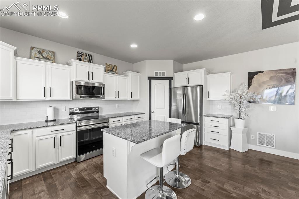 Image 11 of 39: Kitchen with decorative backsplash, stainless steel appliances, white cabin