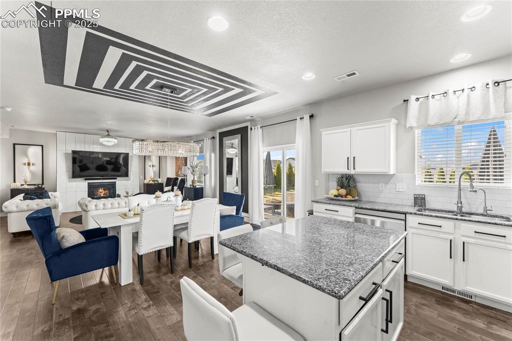 Image 12 of 39: Kitchen with dark stone countertops, white cabinets, open floor plan, a fir