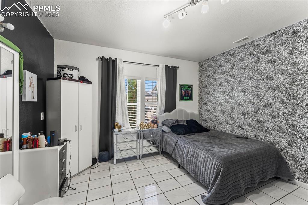 Image 16 of 39: Bedroom featuring wallpapered walls, an accent wall, light tile patterned f