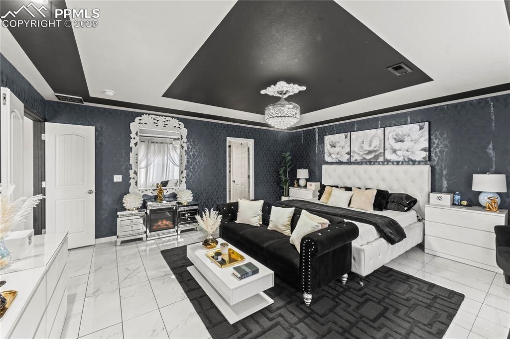 Image 23 of 39: Bedroom with a tray ceiling and wallpapered walls