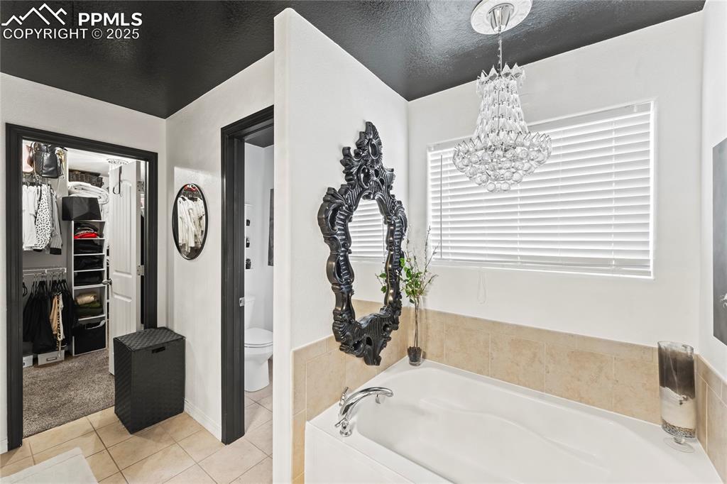 Image 26 of 39: Bathroom with a walk in closet, tile patterned floors, a bath, a textured c