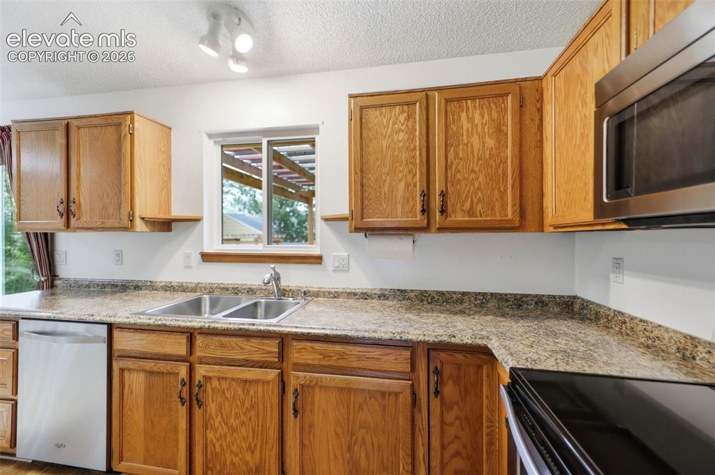 Image 14 of 50: Kitchen featuring wood cabinetry, granite-patterned countertops, a double b