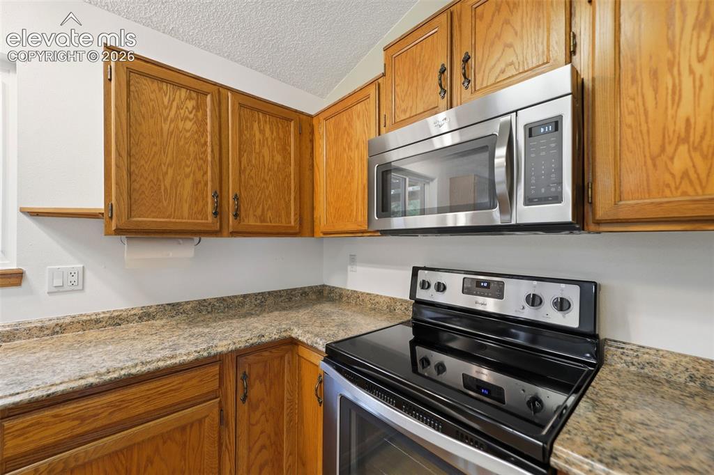 Image 15 of 50: Kitchen featuring wood cabinetry, stainless steel microwave, black electric