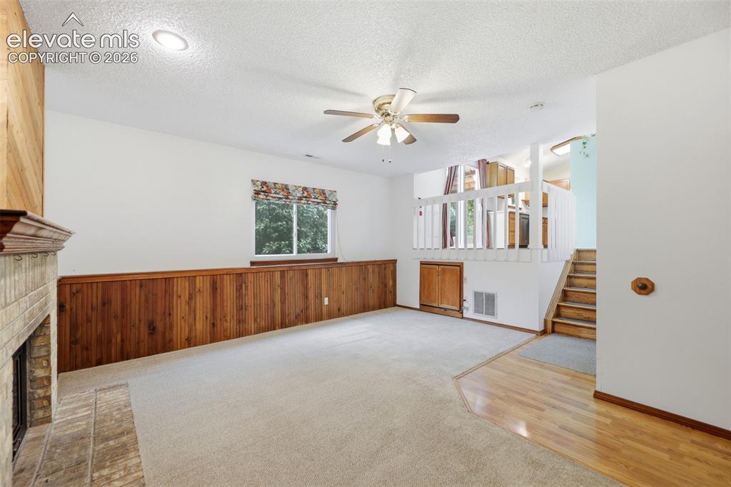 Image 21 of 50: Spacious room featuring a brick fireplace with wood mantel, wood paneling,