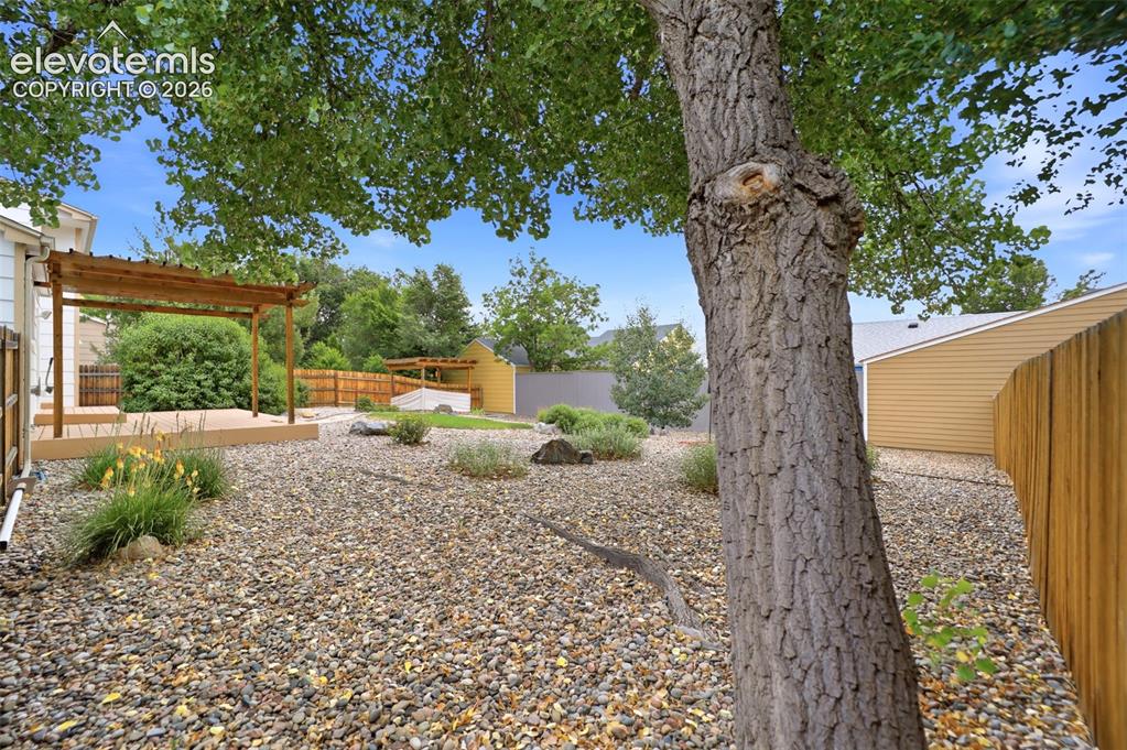Image 37 of 50: Expansive gravel landscaping featuring a wooden deck with a pergola, mature