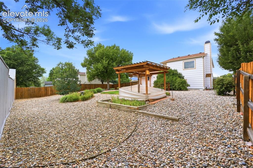 Image 41 of 50: Expansive backyard featuring a gravel landscape, a wooden pergola over a de