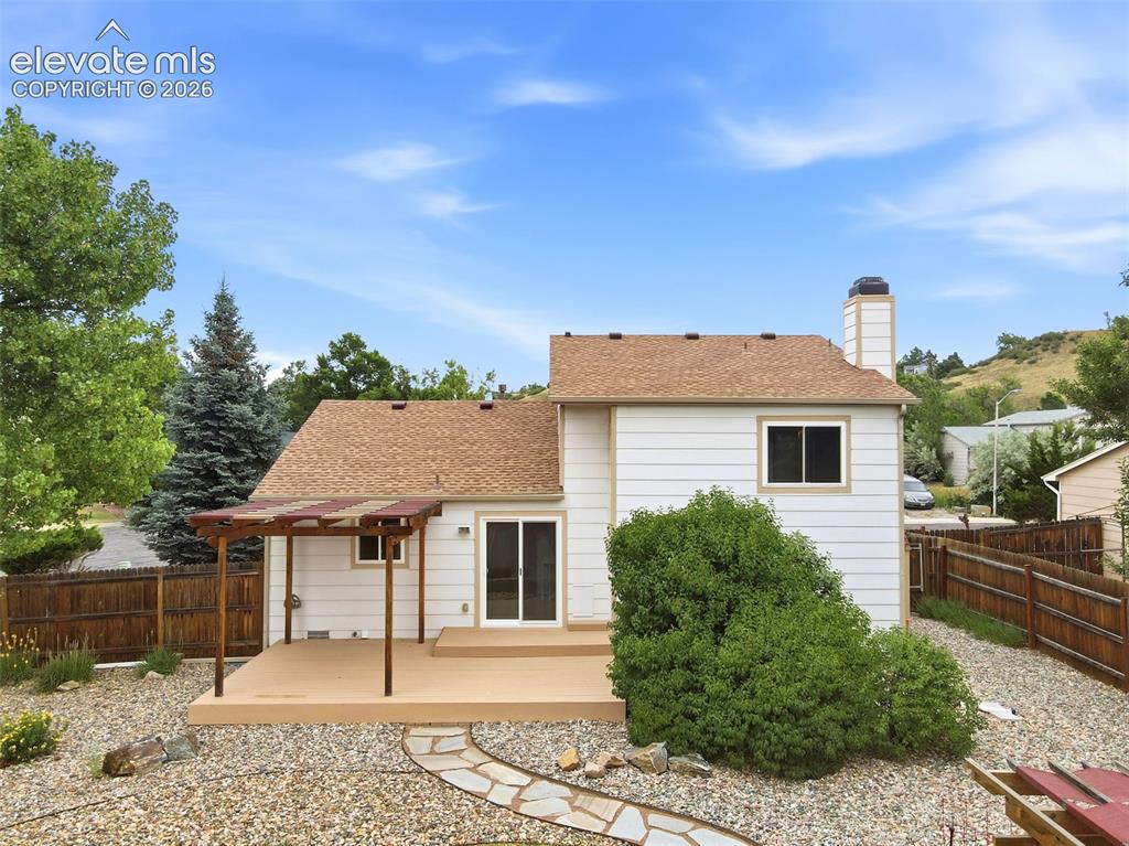Image 45 of 50: Backyard featuring a ground-level deck with a pergola, stone pathway, and g