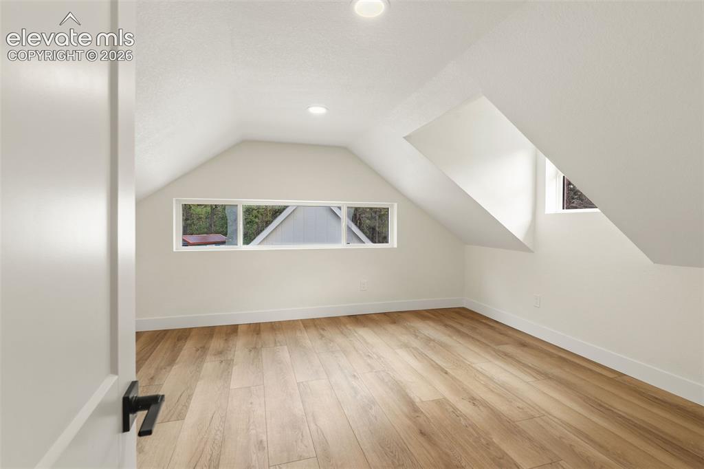 Image 25 of 43: Bedroom with character, featuring vaulted ceiling, light wood finished floo