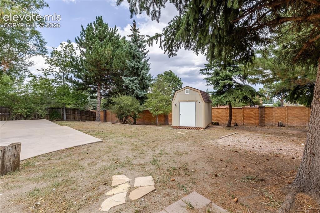 Image 11 of 46: Expansive backyard featuring a concrete patio, mature trees, a storage shed