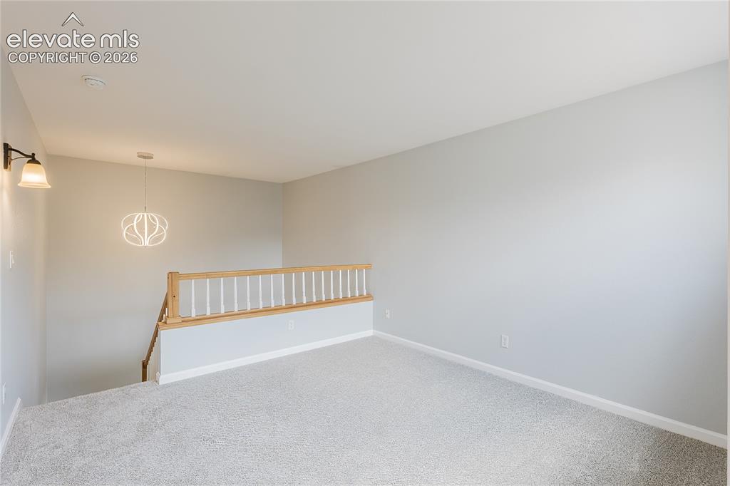 Image 20 of 46: Carpeted loft area with a wood and white spindle railing, modern pendant li