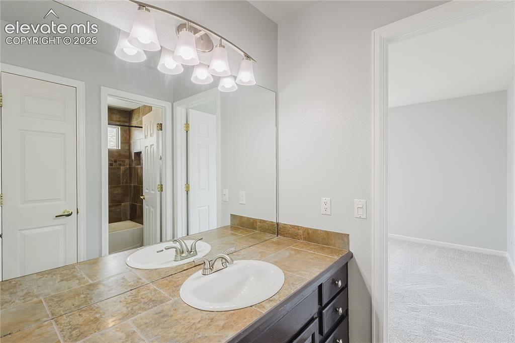 Image 27 of 46: Dual vanity with integrated sinks, tiled countertop, and track lighting