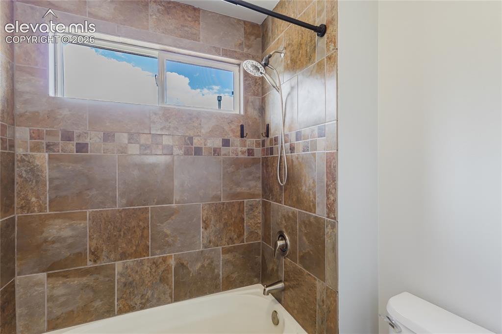Image 28 of 46: Bathtub with a tiled surround featuring a decorative accent band and a show