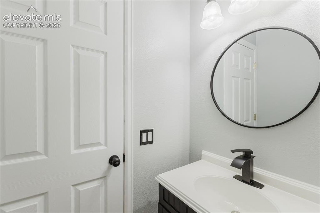 Image 35 of 46: White paneled door with a black doorknob, black framed round mirror, and a 