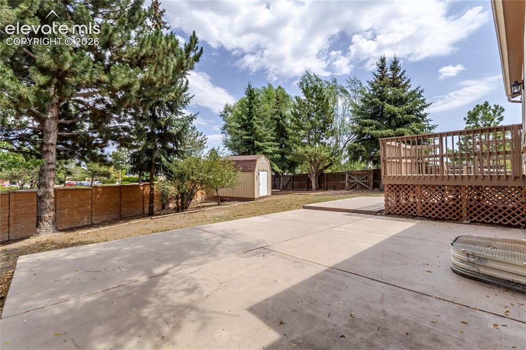 Image 4 of 46: Expansive concrete patio with a raised wooden deck featuring lattice skirti