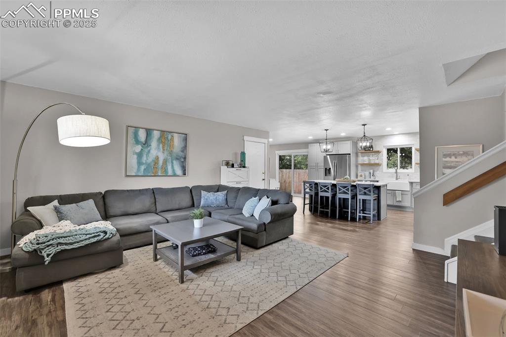 Image 14 of 50: Living room featuring stairway, dark wood-style floors, and a chandelier