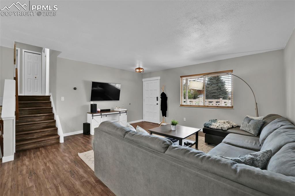 Image 16 of 50: Living room featuring dark wood-style flooring, stairs, and a textured ceil
