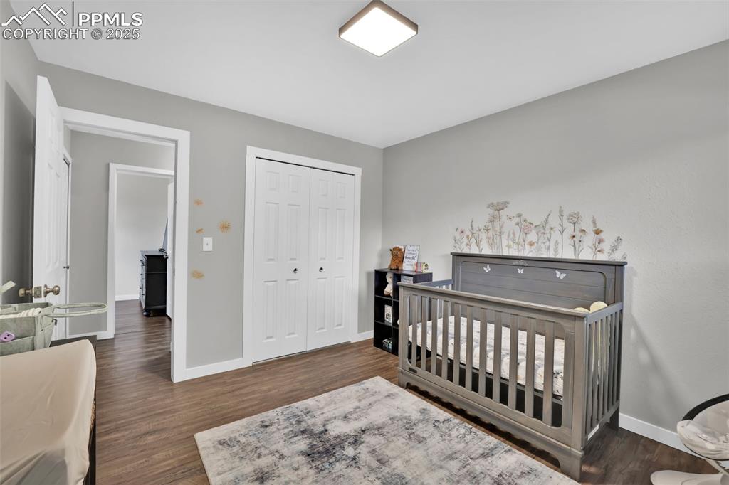 Image 28 of 50: Bedroom featuring a nursery area, dark wood-style flooring, and a closet