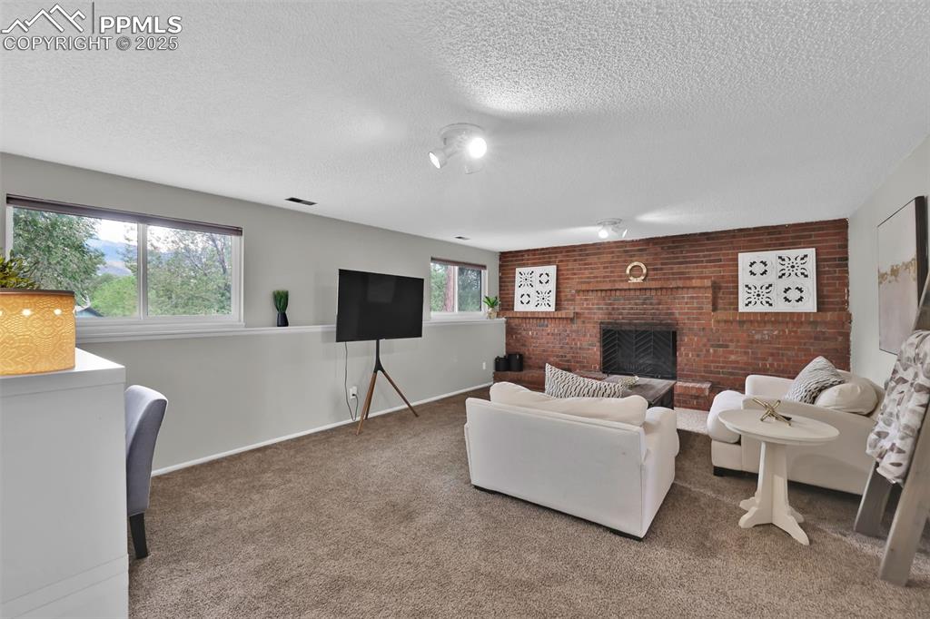 Image 32 of 50: Living room with carpet, brick wall, a brick fireplace, and a textured ceil