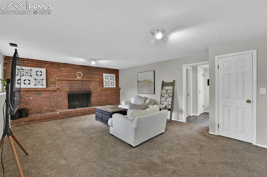 Image 33 of 50: Living room with carpet flooring, a textured ceiling, a fireplace, and bric