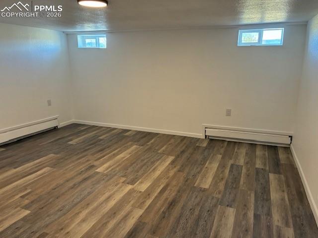 Image 18 of 36: Basement with dark wood-style floors, a baseboard radiator, and a textured