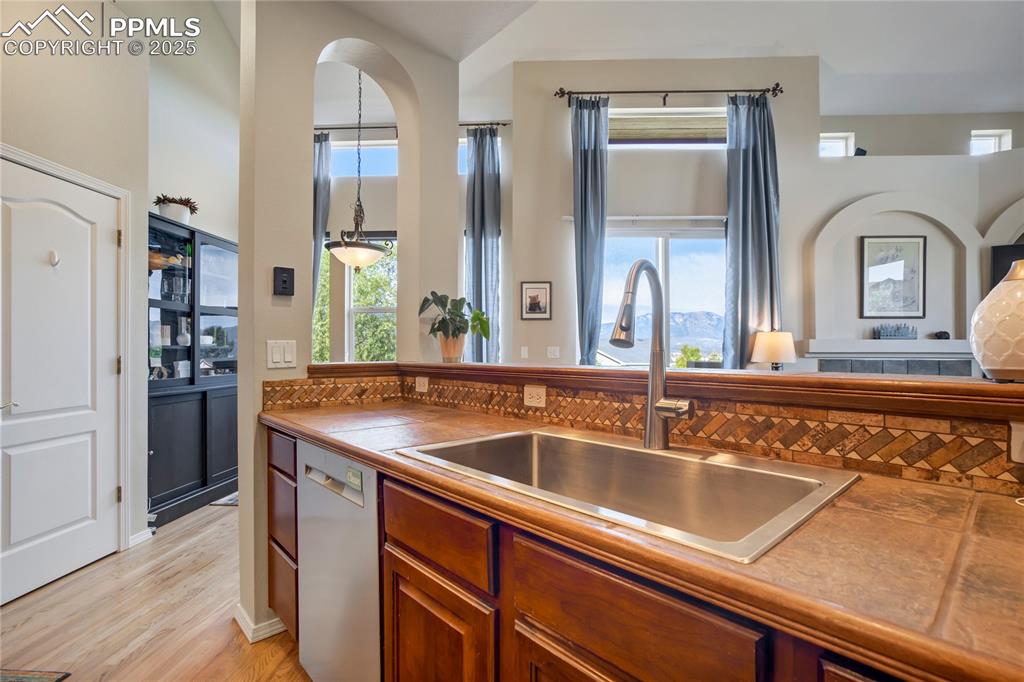 Image 10 of 43: Kitchen with brown cabinets, stainless steel dishwasher, light wood-style f