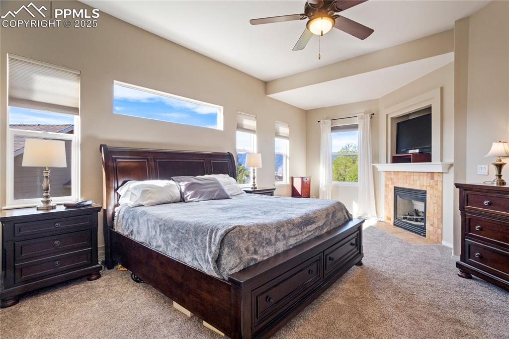 Image 18 of 43: Bedroom featuring light colored carpet, ceiling fan, and a fireplace